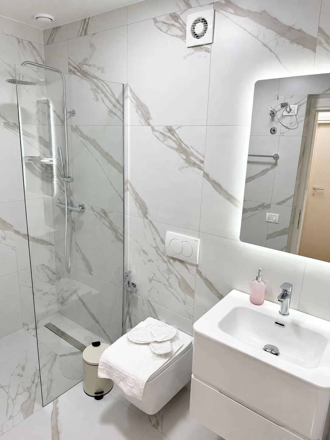 Bathroom with walk-in glass shower, backlit mirror, washbasin and marble-effect tiles