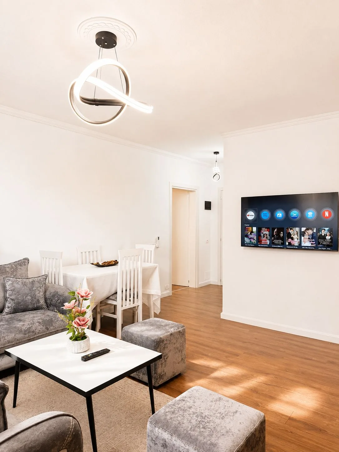 Dining table with white chairs and a wall-mounted smart TV in the living area