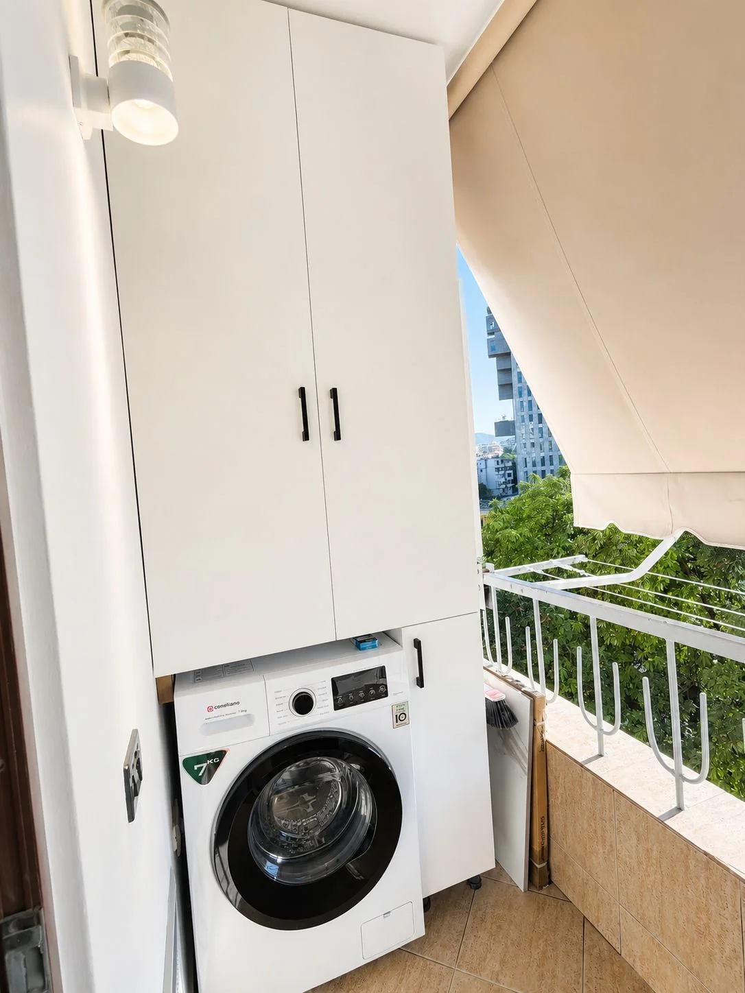 Balcony with washing machine, storage cupboard, drying rack, awning and a green outlook over Tirana