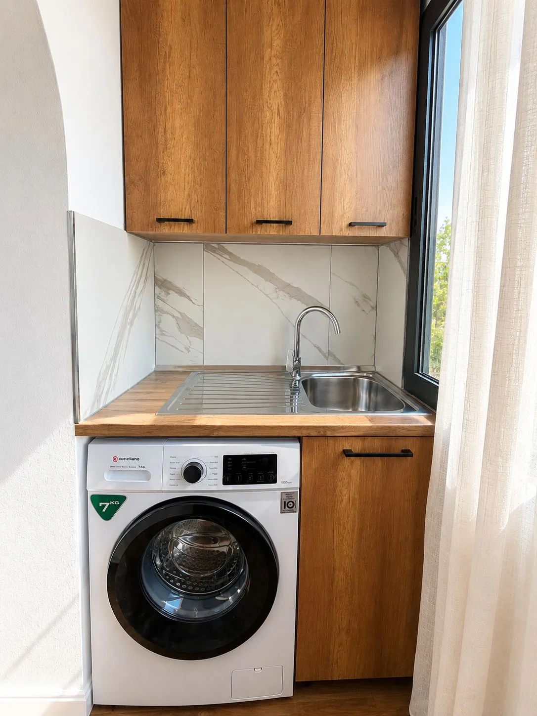 Utility area with a 7 kg washing machine, sink and wooden cabinets next to the window