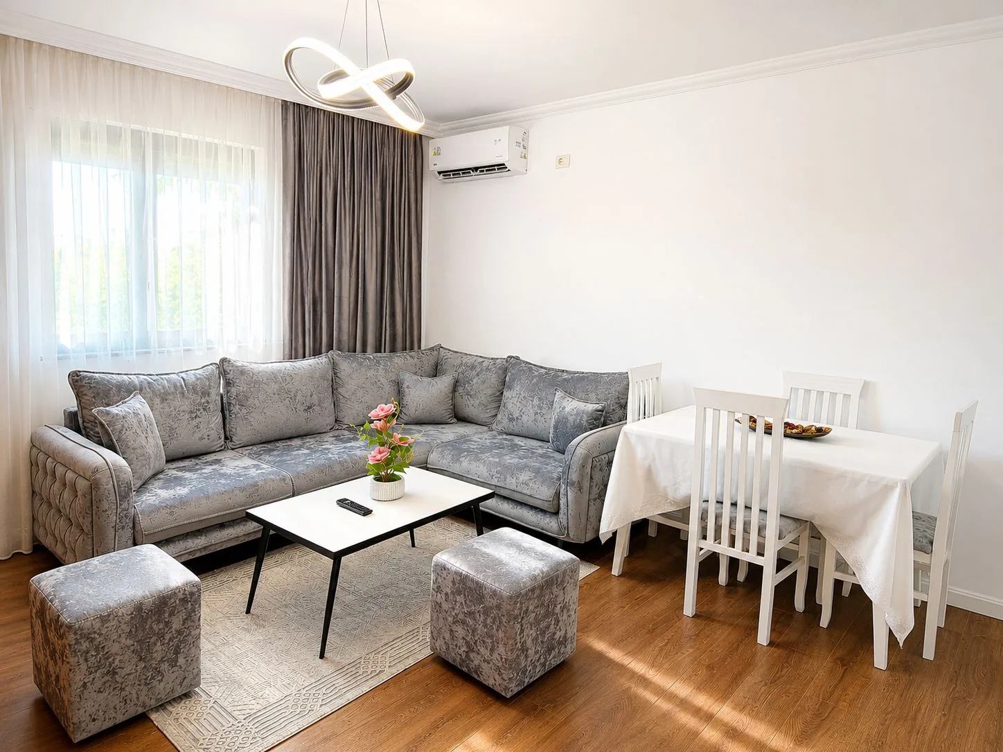 Living area of the studio apartment in Tirana with a large grey corner sofa, dining table and air conditioning