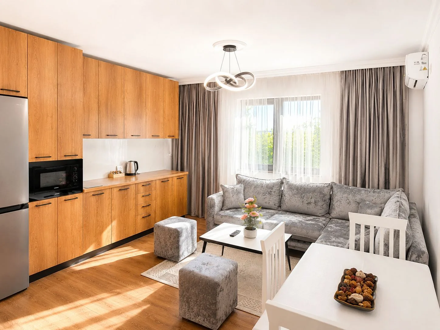 Open-plan kitchen and living room with oak cabinets, fridge, microwave, corner sofa and bright windows